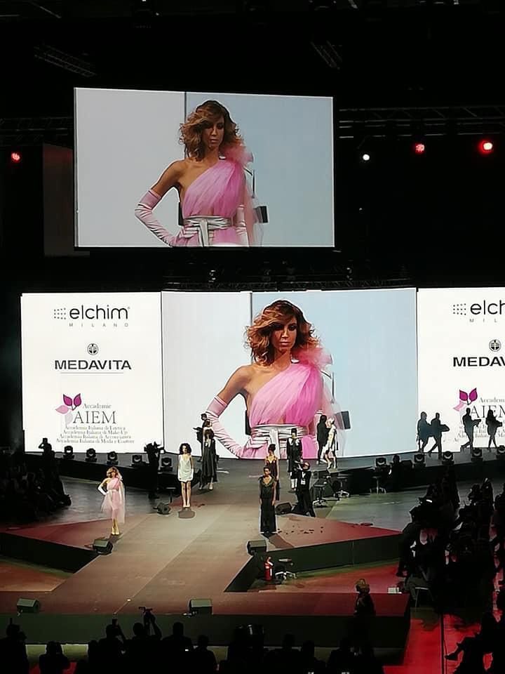 Una donna con un vestito rosa sta sfilando sulla passerella durante una sfilata di moda.