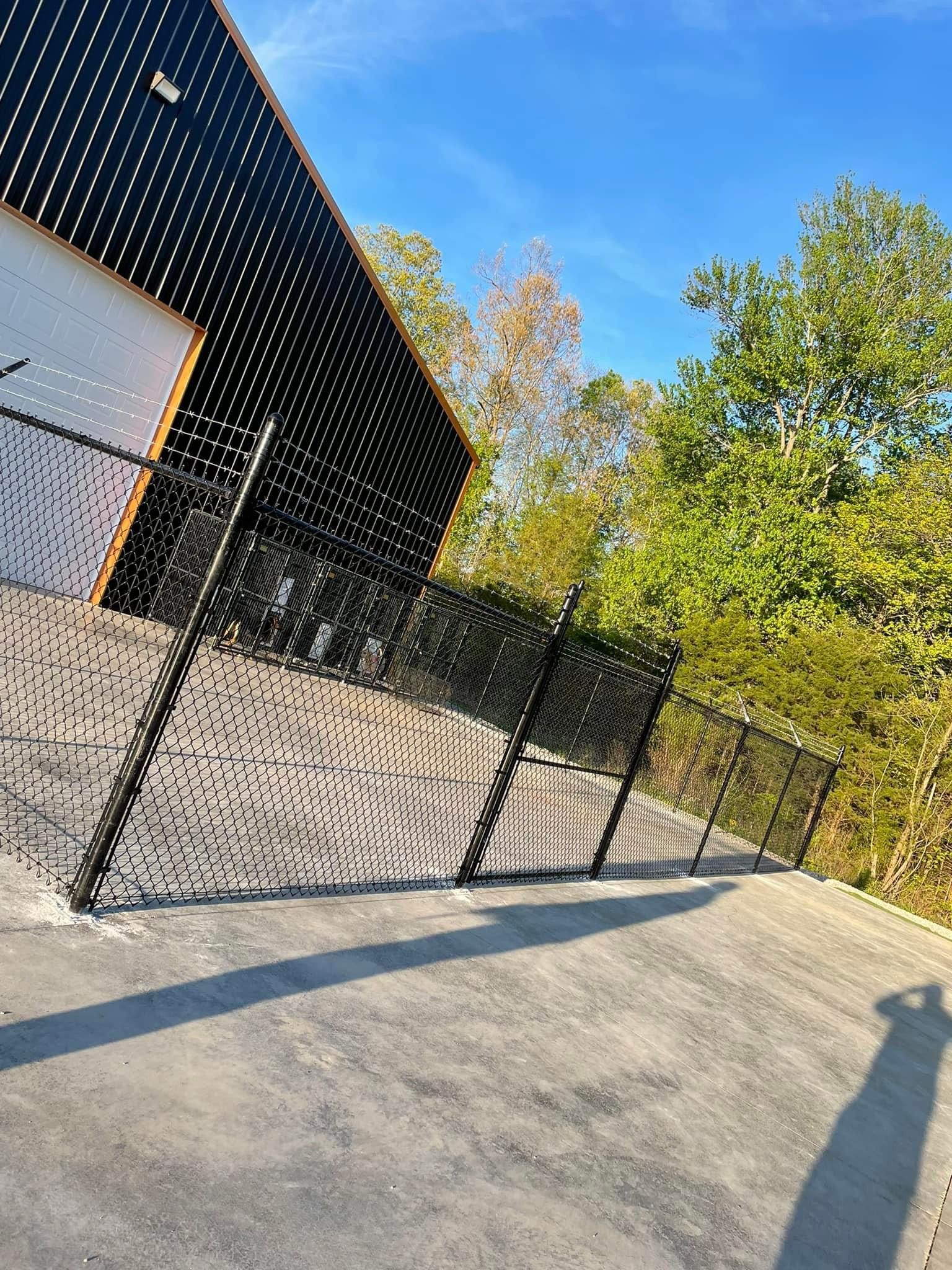 A chain link fence surrounds a concrete walkway in front of a building.