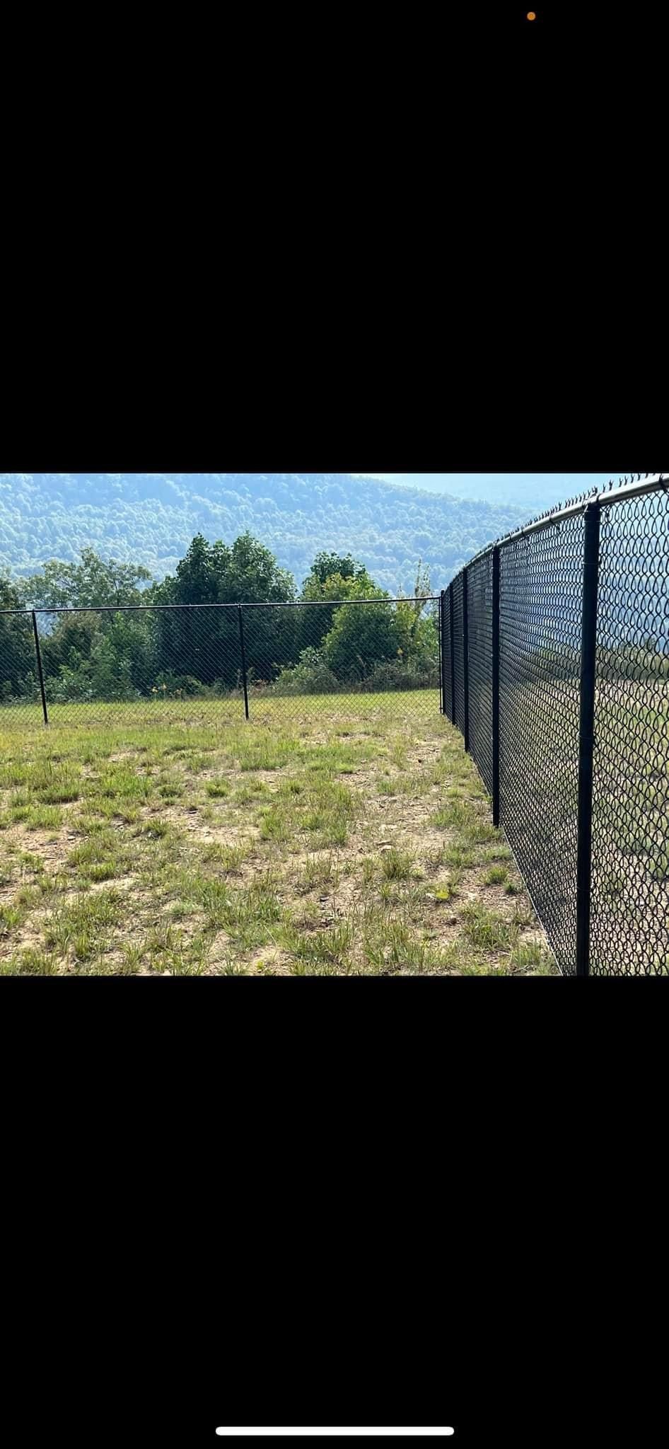 A chain link fence surrounds a grassy field with trees in the background.