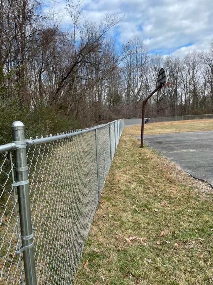 A chain link fence surrounds a basketball hoop in a park.