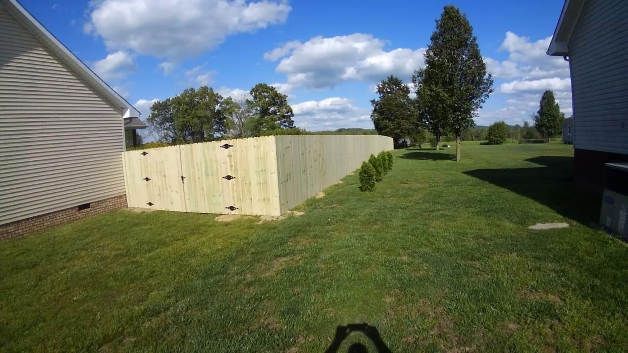 A wooden fence is sitting in the middle of a lush green yard next to a house.