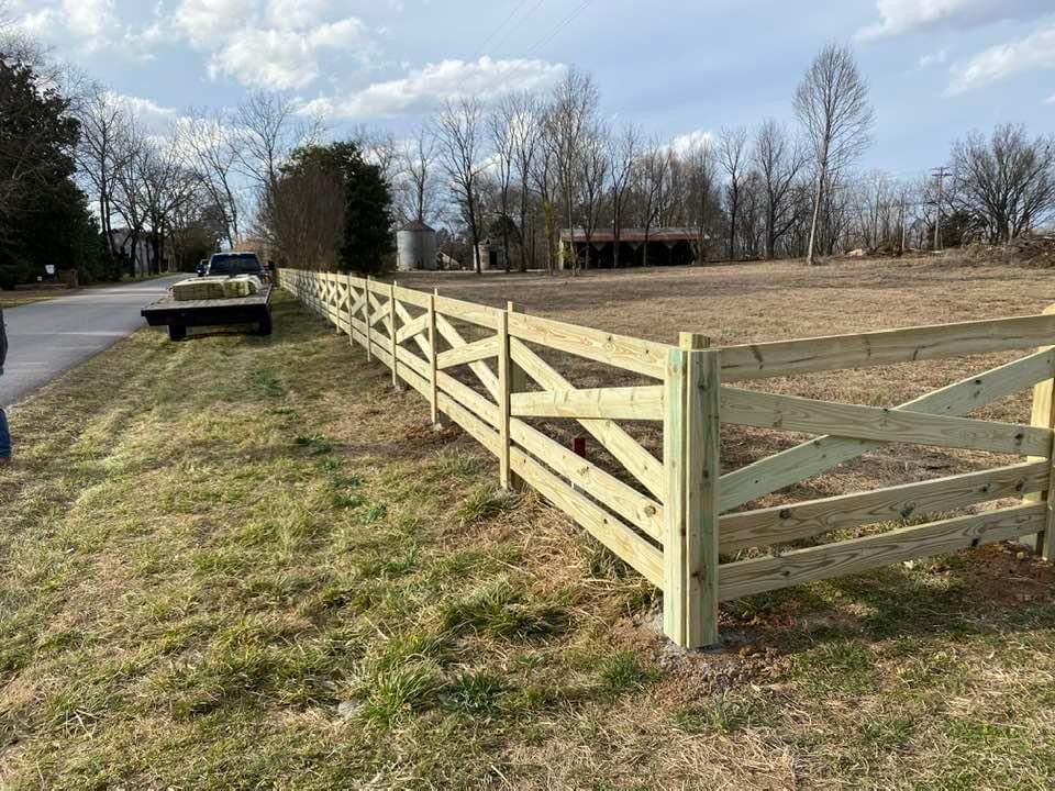 A wooden fence is sitting in the middle of a grassy field next to a road.
