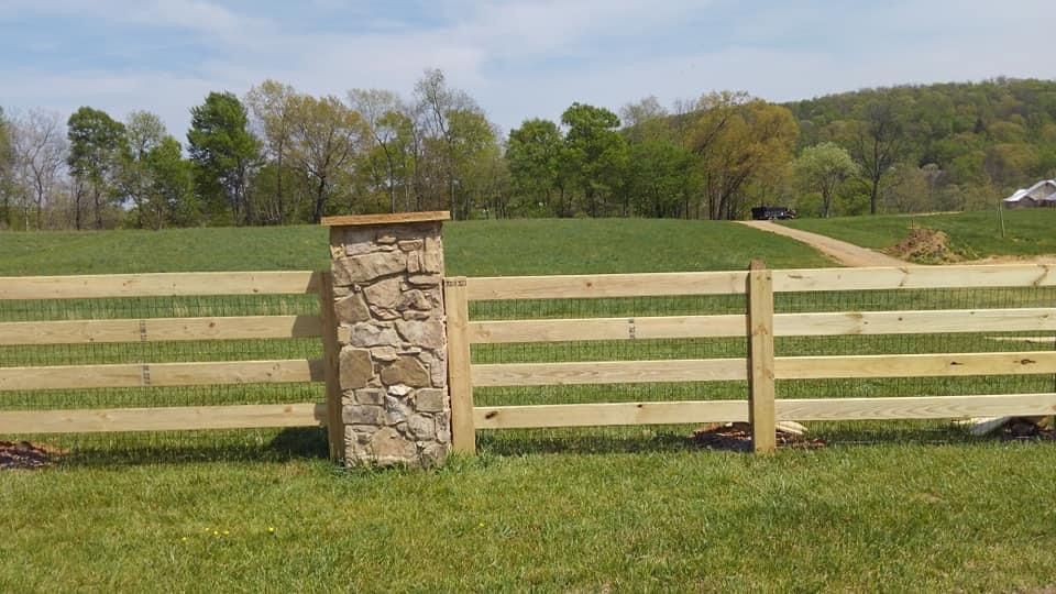 A wooden fence with a stone pillar in the middle of a grassy field.