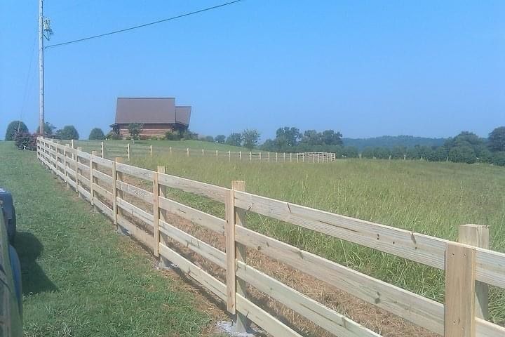 A wooden fence surrounds a grassy field with a house in the background.