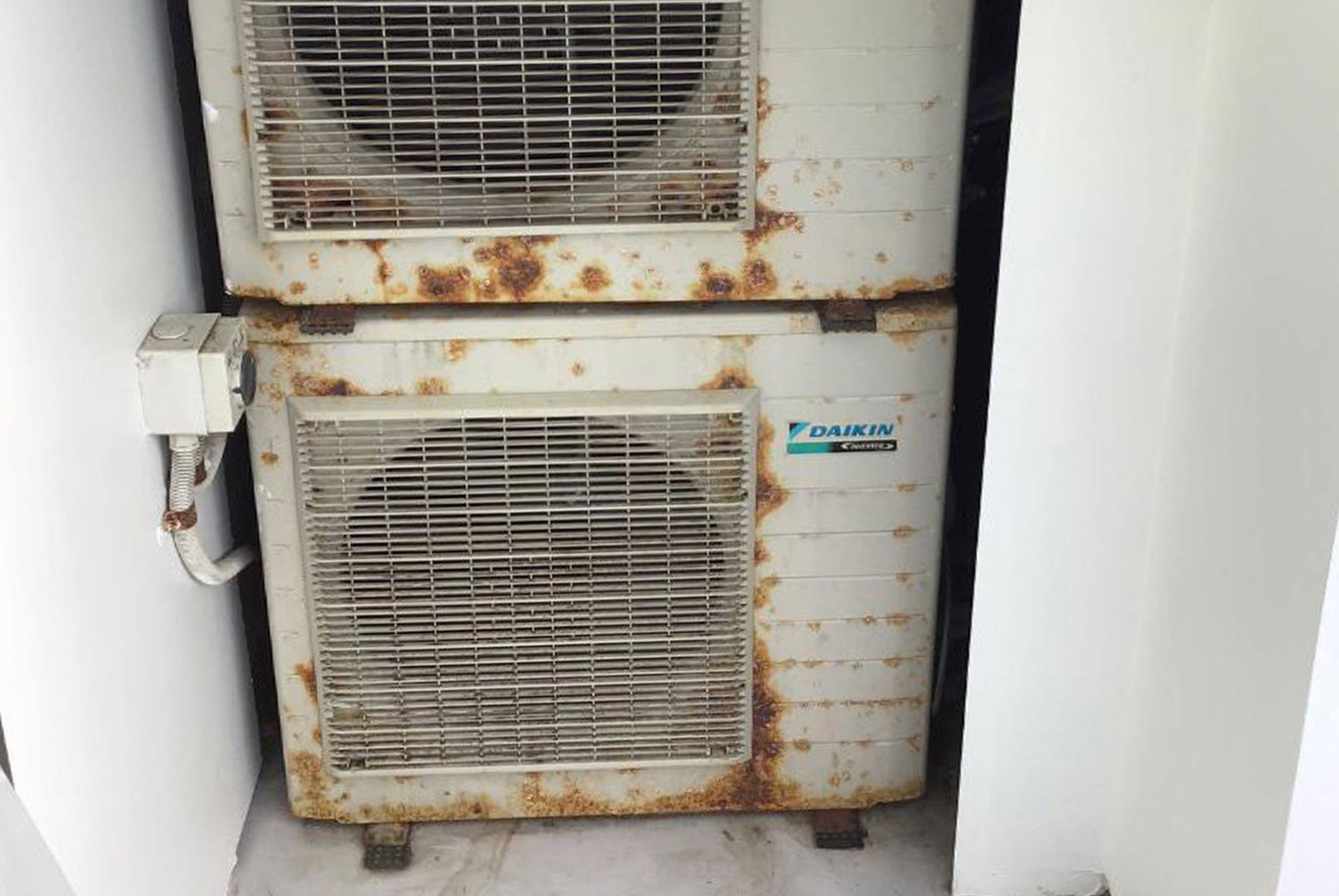 Two rusty air conditioners are stacked on top of each other.