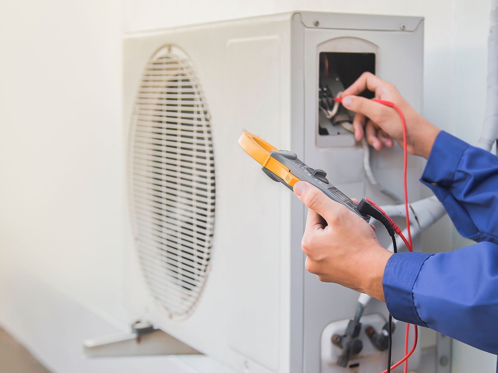 A man is using a voltmeter to test an air conditioner.