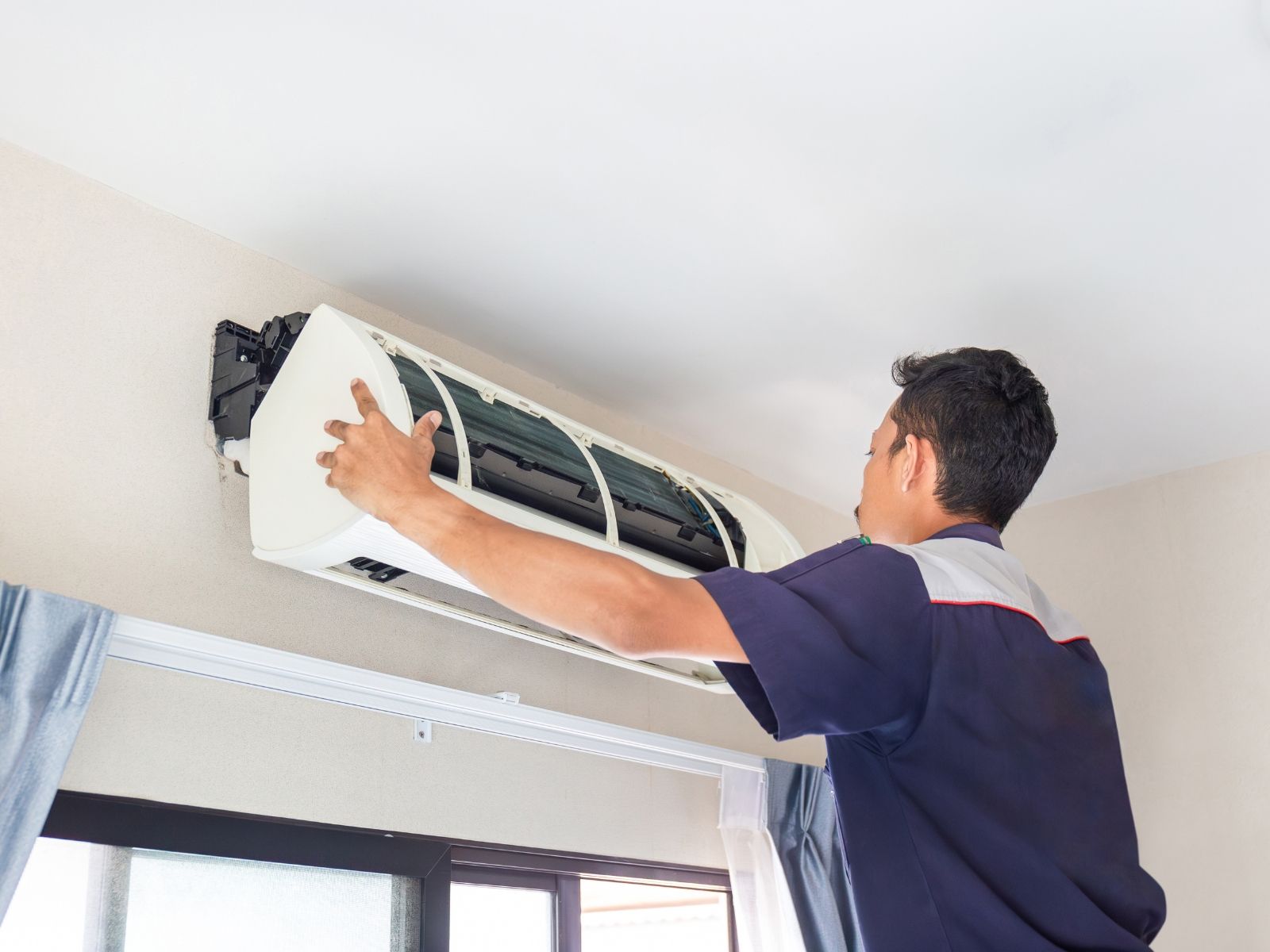 A man is fixing an air conditioner in a living room.