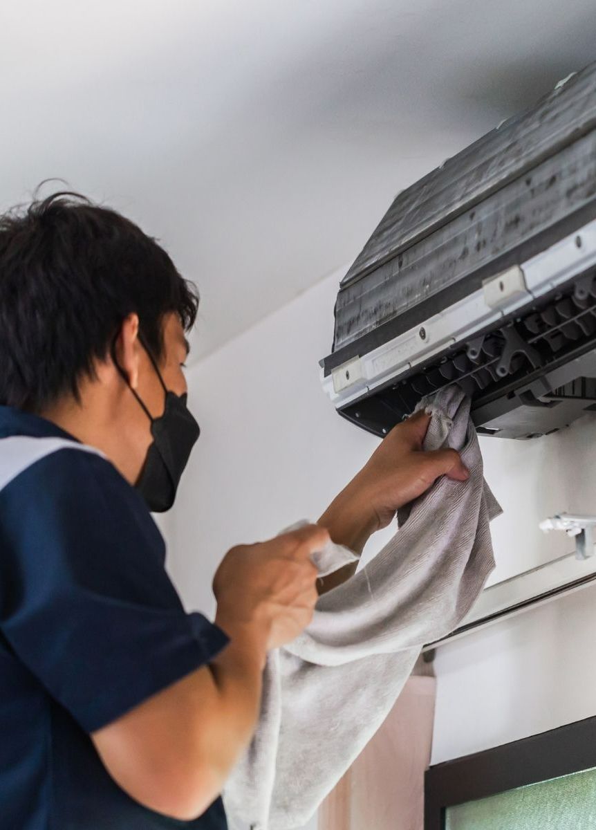 A man wearing a mask is cleaning an air conditioner with a towel.