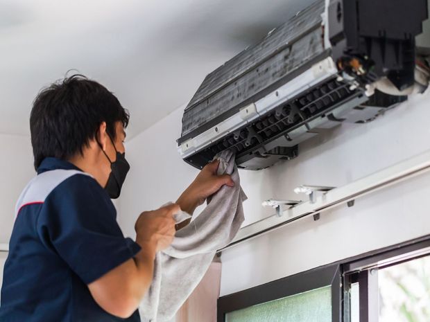 A man wearing a mask is cleaning an air conditioner with a towel.