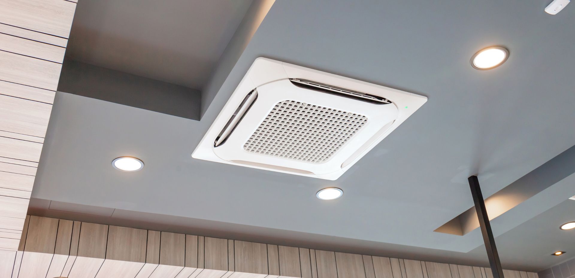A square air conditioner is hanging from the ceiling of a room.