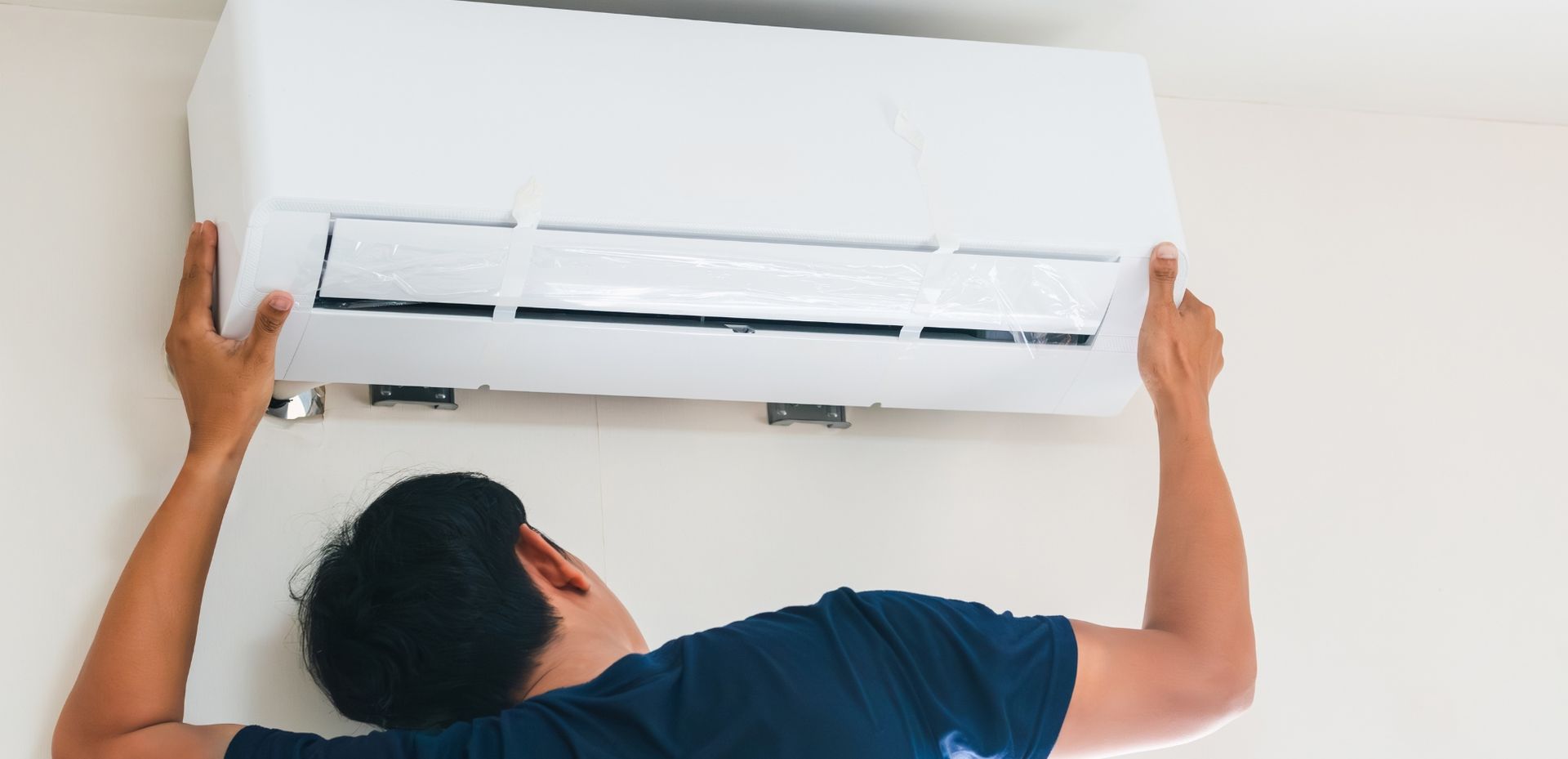 A man is installing an air conditioner on the wall.