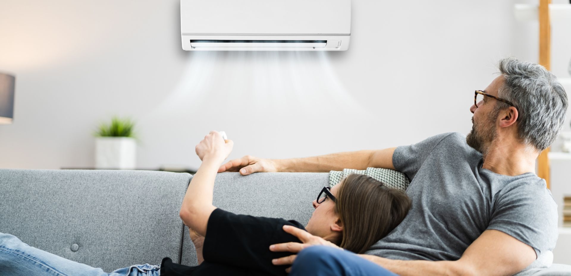 A man and a child are laying on a couch under an air conditioner.