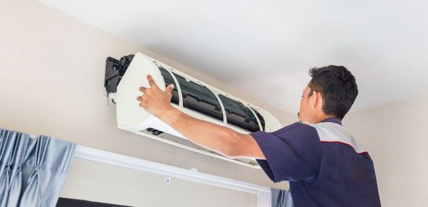 A man is cleaning an air conditioner in a living room.