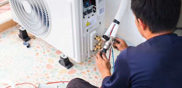 A man is sitting on the floor fixing an air conditioner.