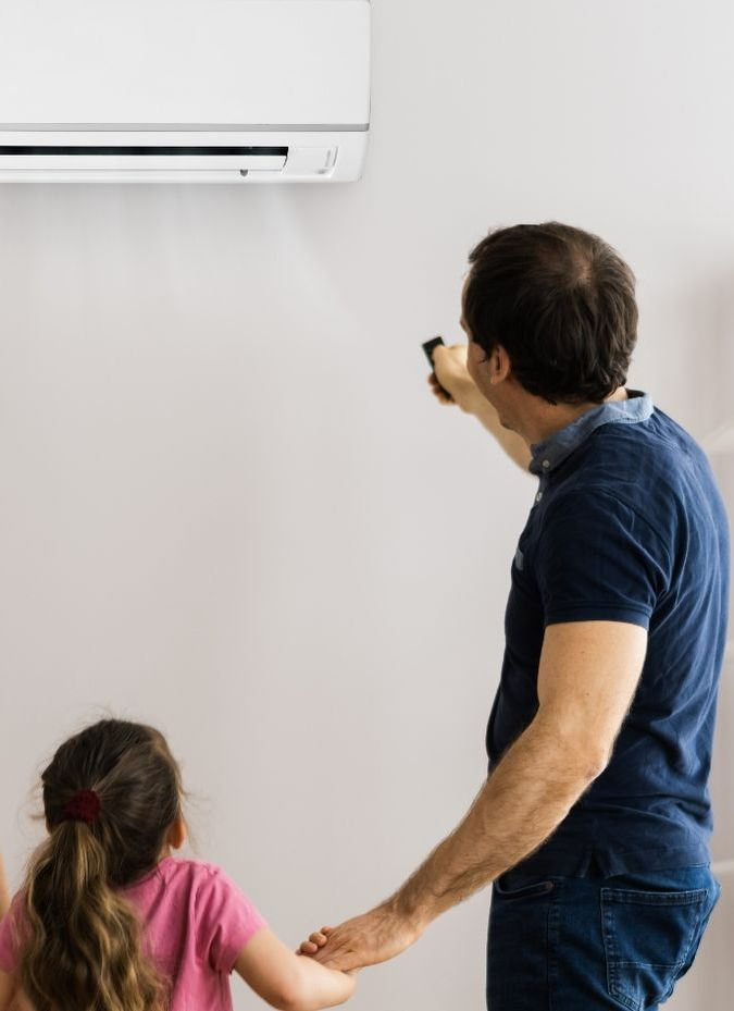 A man and a little girl are standing in front of an air conditioner.