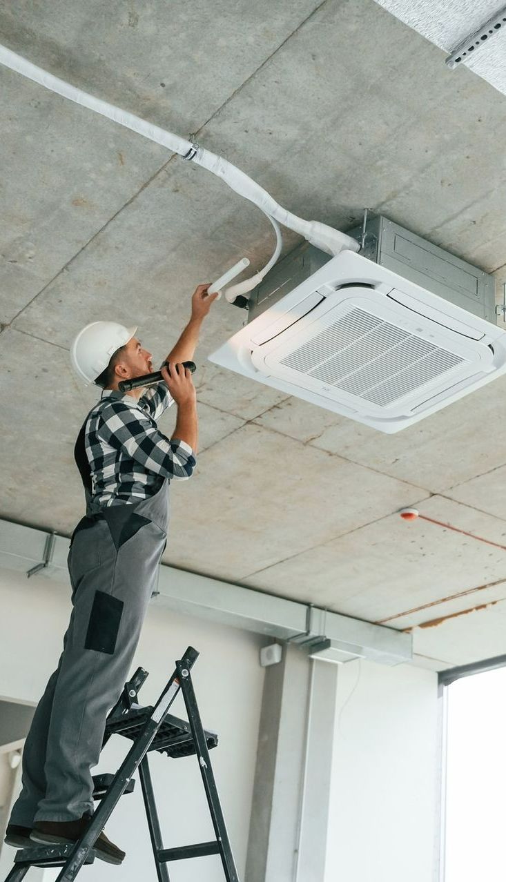 A man is standing on a ladder fixing a ceiling fan.