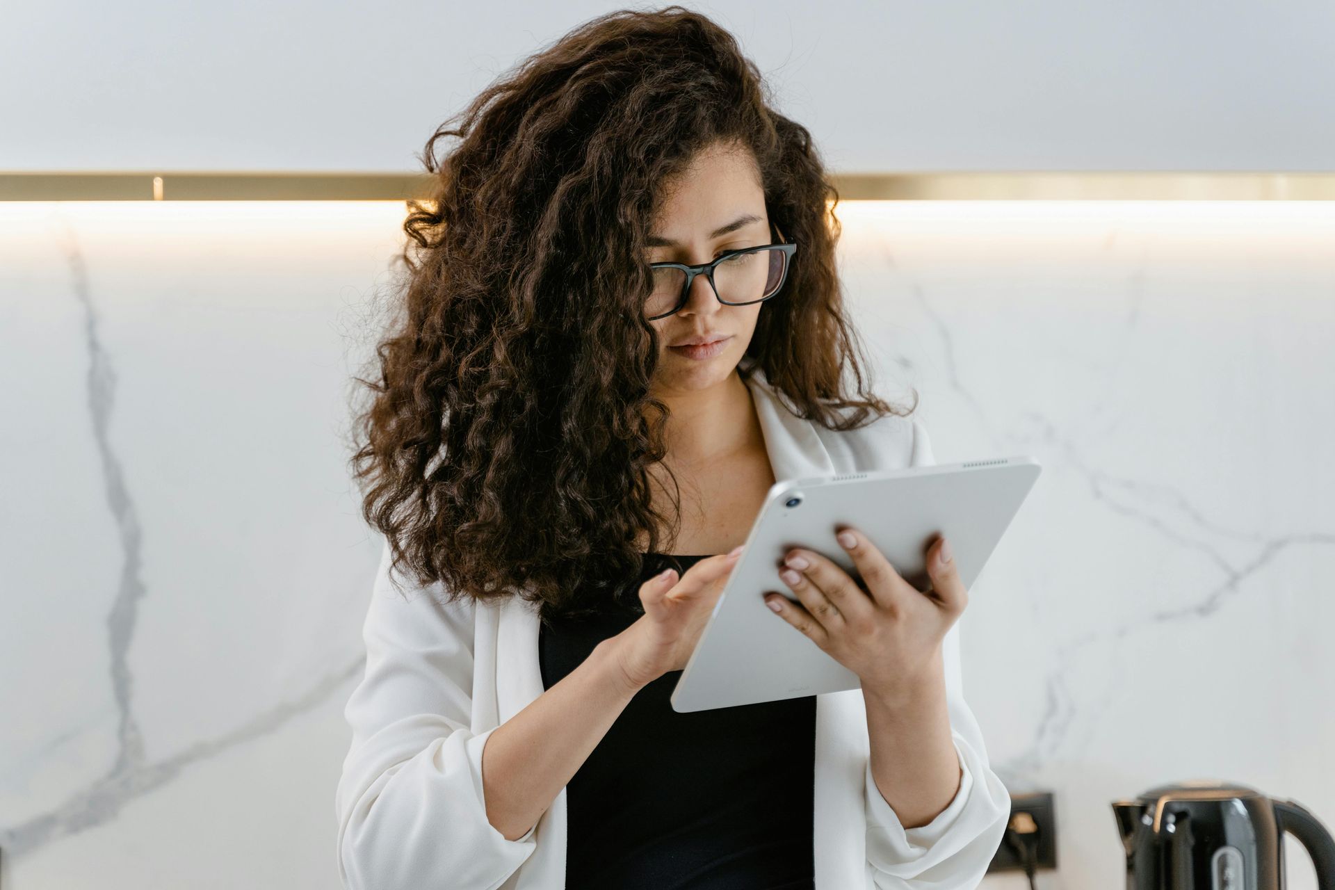 A woman wearing glasses is using a tablet computer in a kitchen.