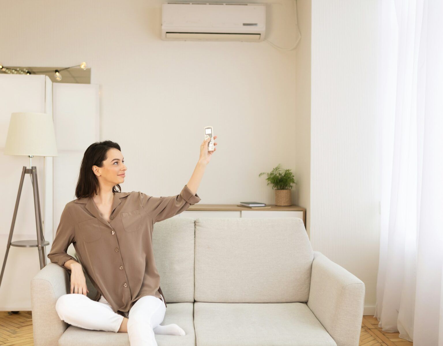 A woman is sitting on a couch in a living room holding a remote control.