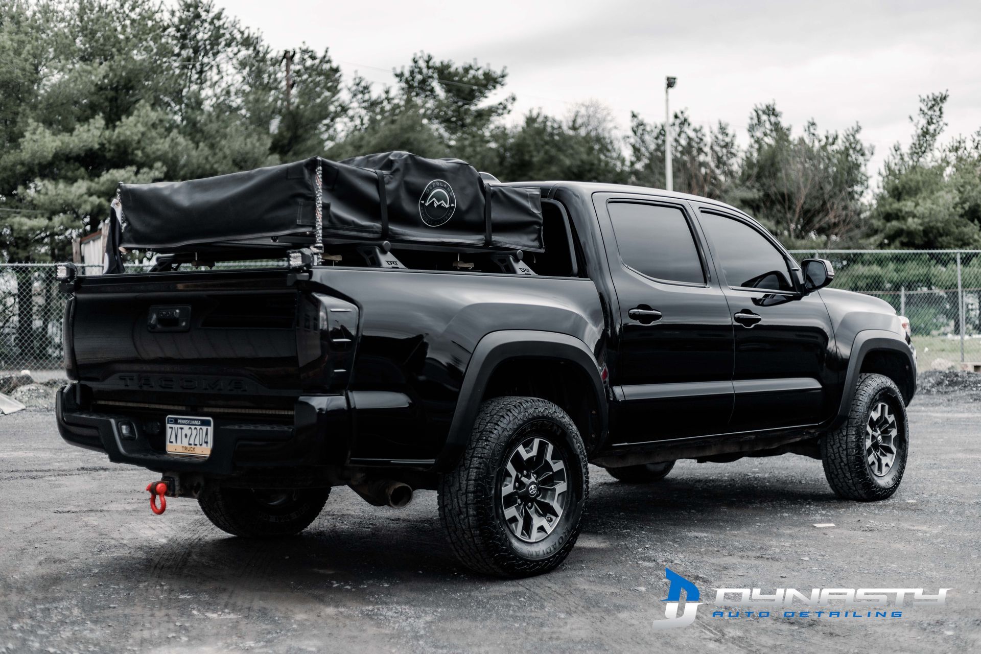A black truck with a tent on top of it is parked in a parking lot.