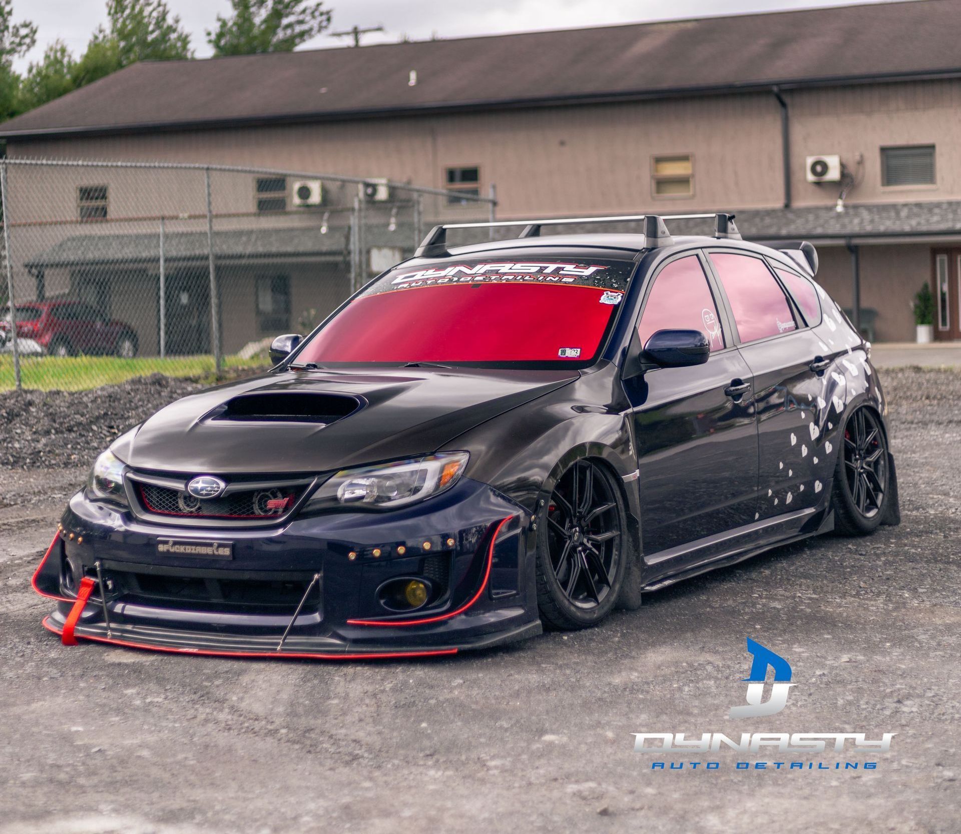 A black car with a red windshield is parked in front of a building.