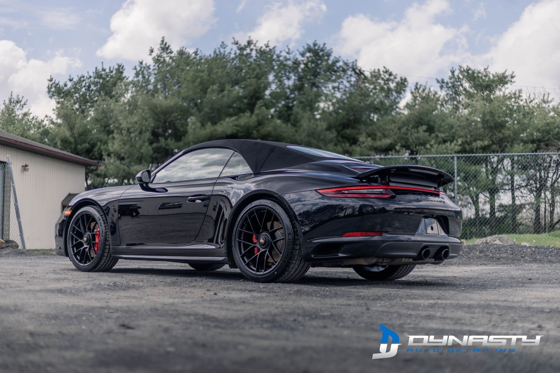 A black porsche 911 convertible is parked in a parking lot.