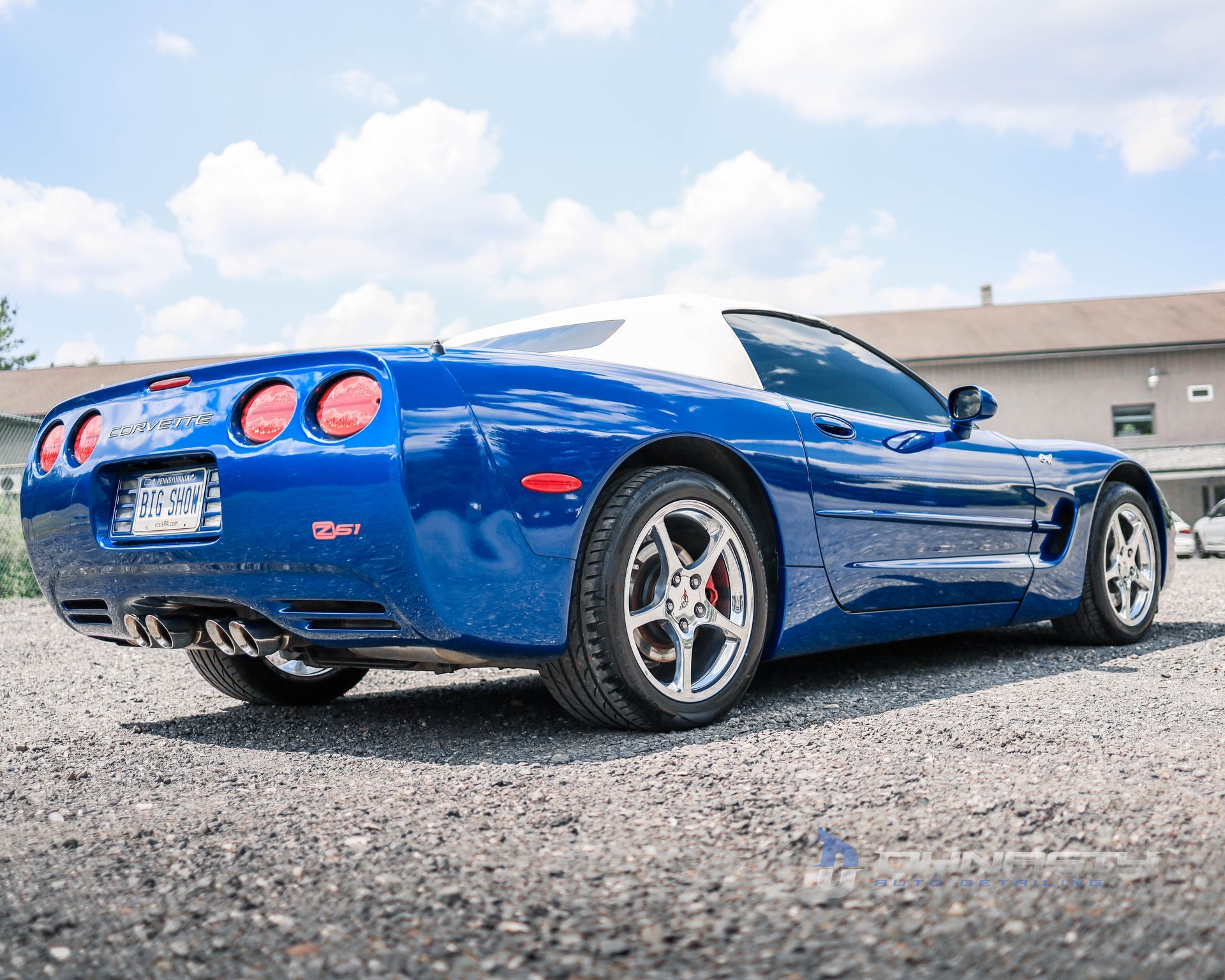 A blue and white sports car is parked in a gravel lot.