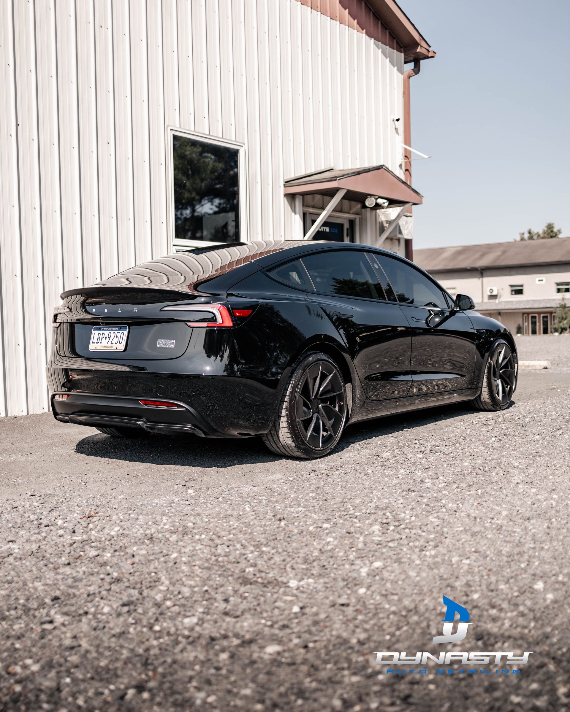 A black tesla model 3 is parked in front of a white building.