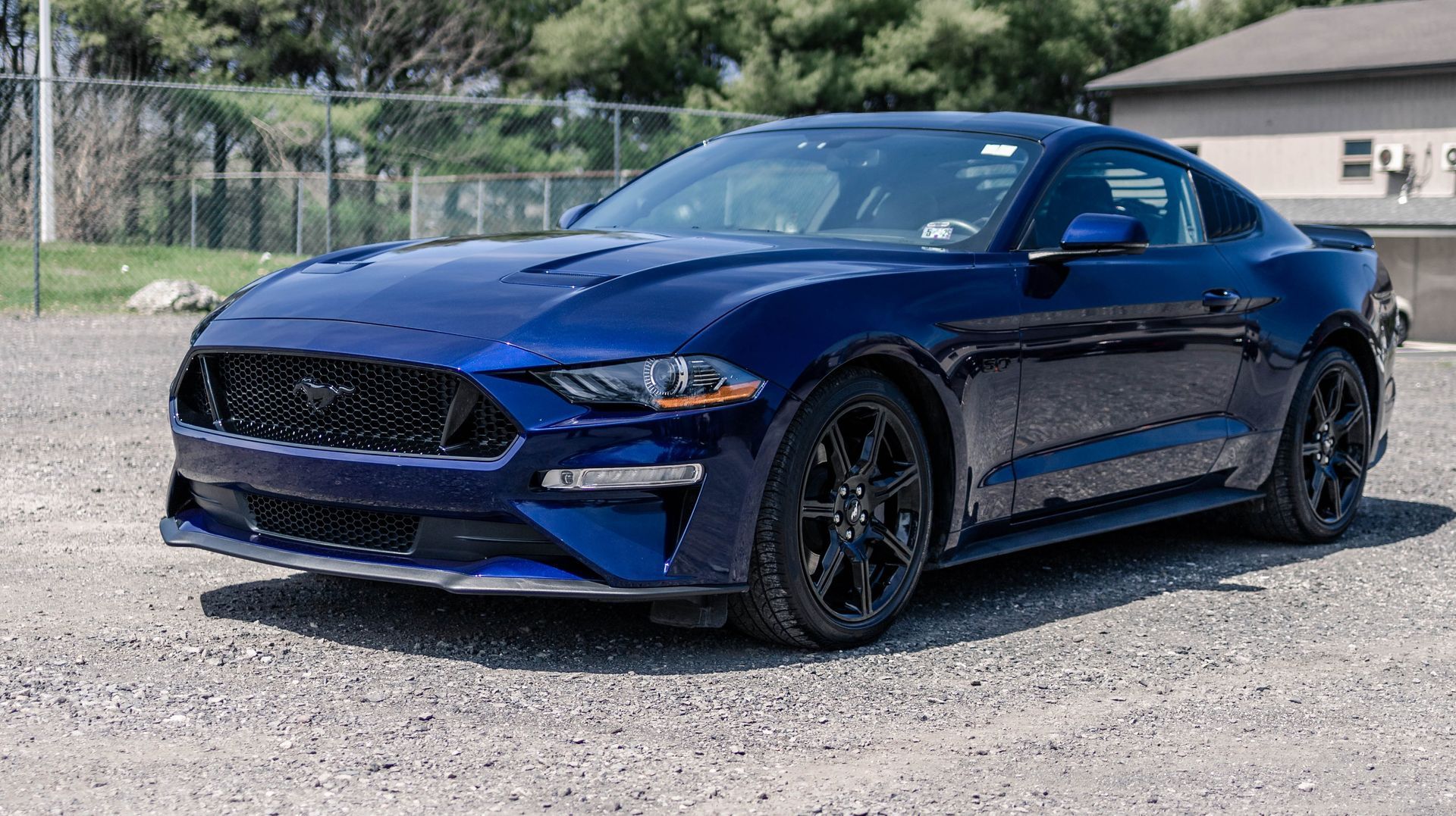 Blue Ford Mustang sports car parked on gravel.