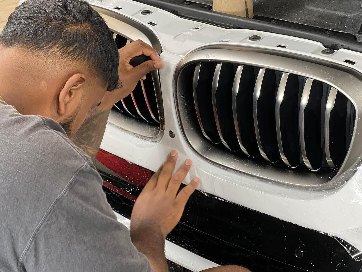 Person applying film to the front of a white car near chrome grill.