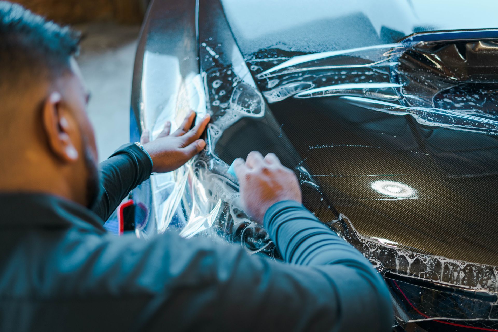 Person applying protective film to a dark vehicle.