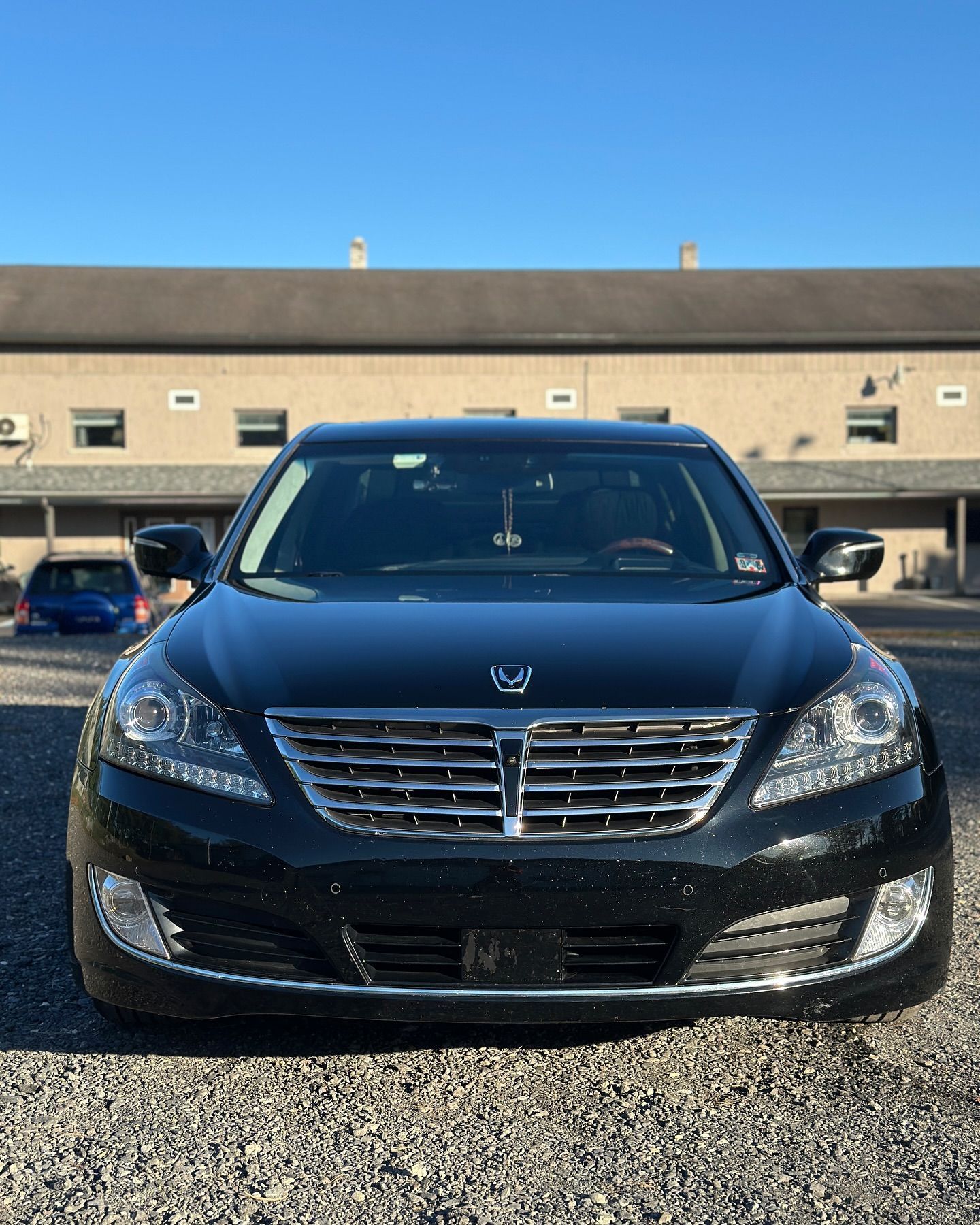 A black car is parked in a gravel lot in front of a building.