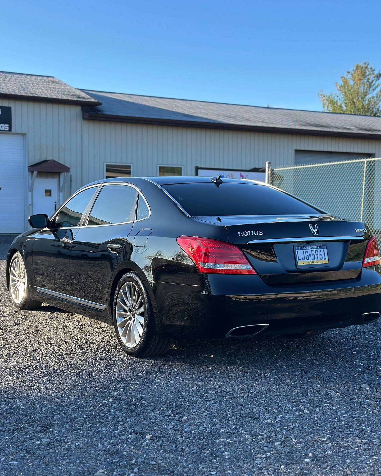 A black car is parked in a gravel lot in front of a building.