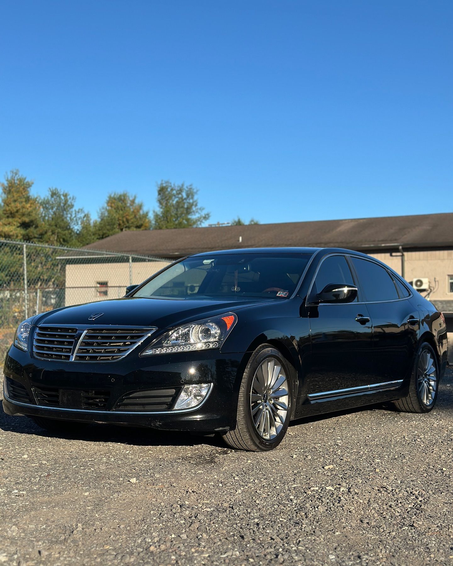 A black car is parked in a gravel lot in front of a building.
