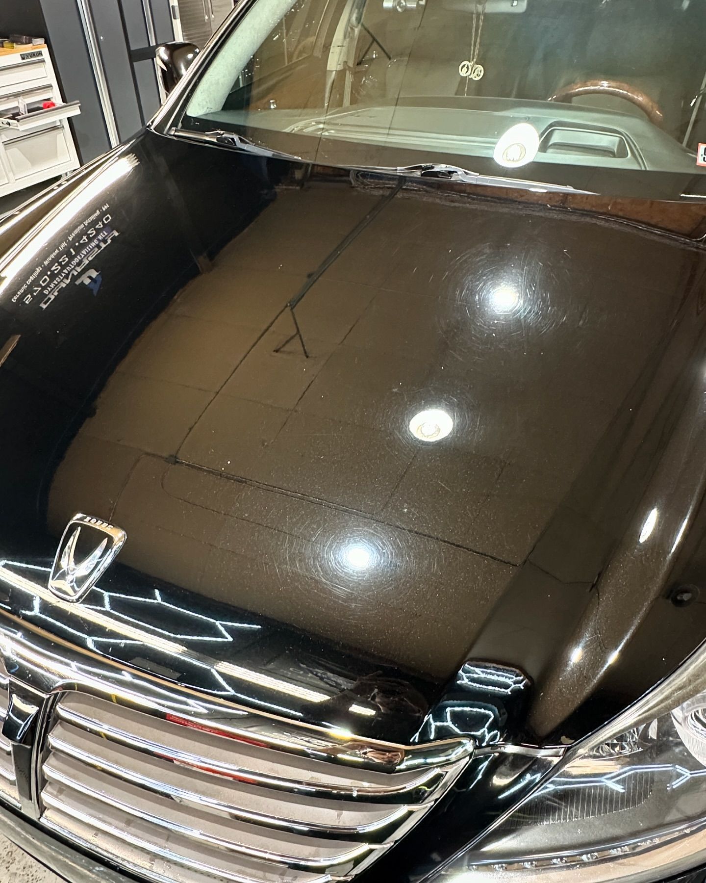 A black car with the hood up is parked in a garage.