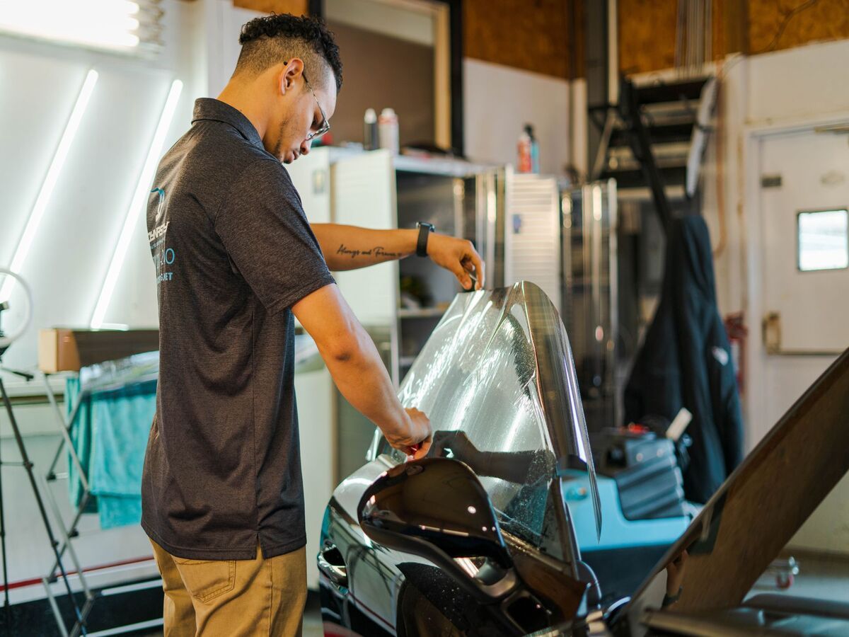 A Dynasty Auto Detailing worker is installing window tint on a car window