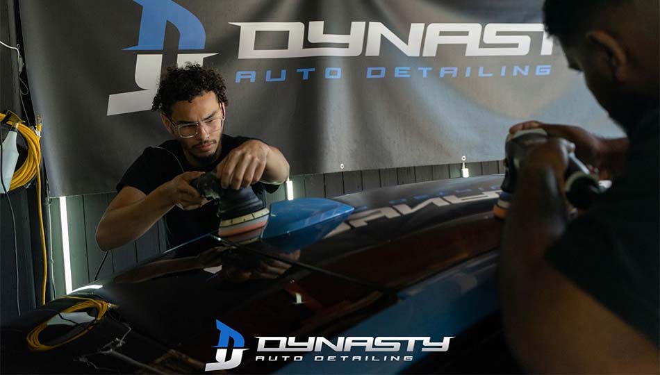 Paint Correction - Two men are polishing a car in front of a dynasty auto detailing banner.