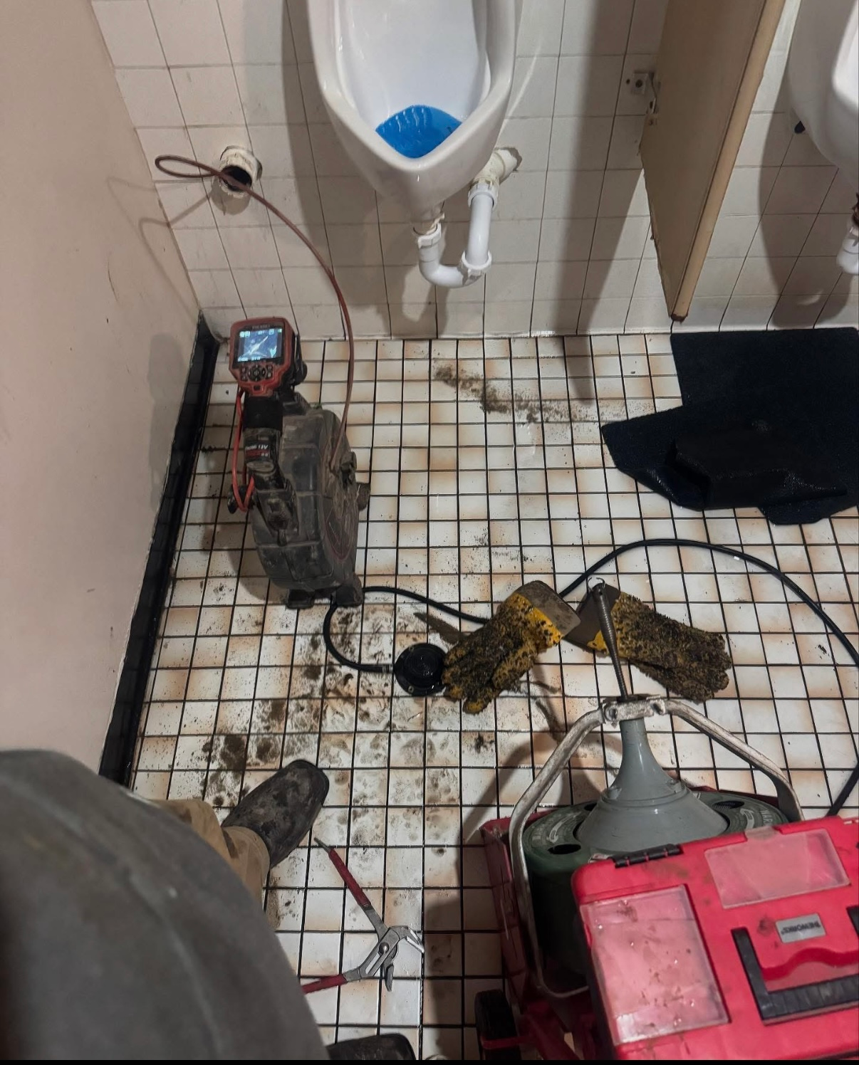 A man is standing in a bathroom next to a urinal.
