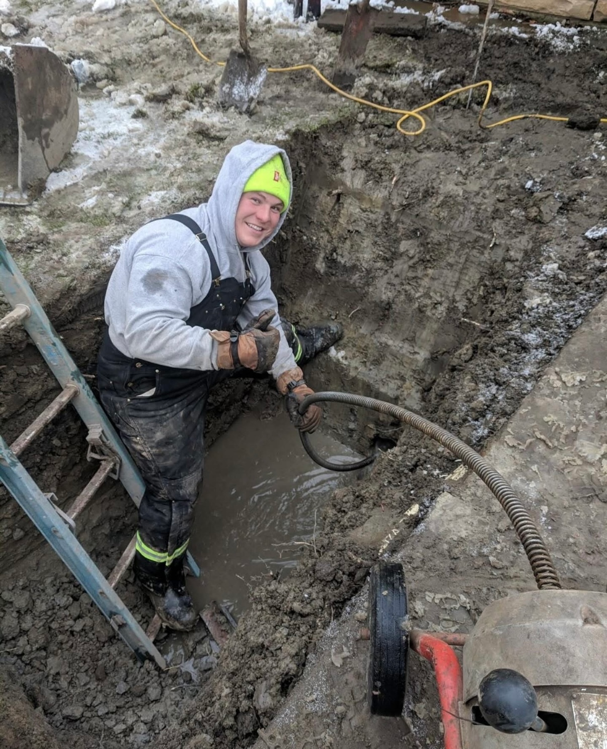 A man is standing in a muddy hole with a ladder.