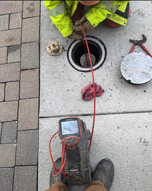 A man in a yellow jacket is working on a drain