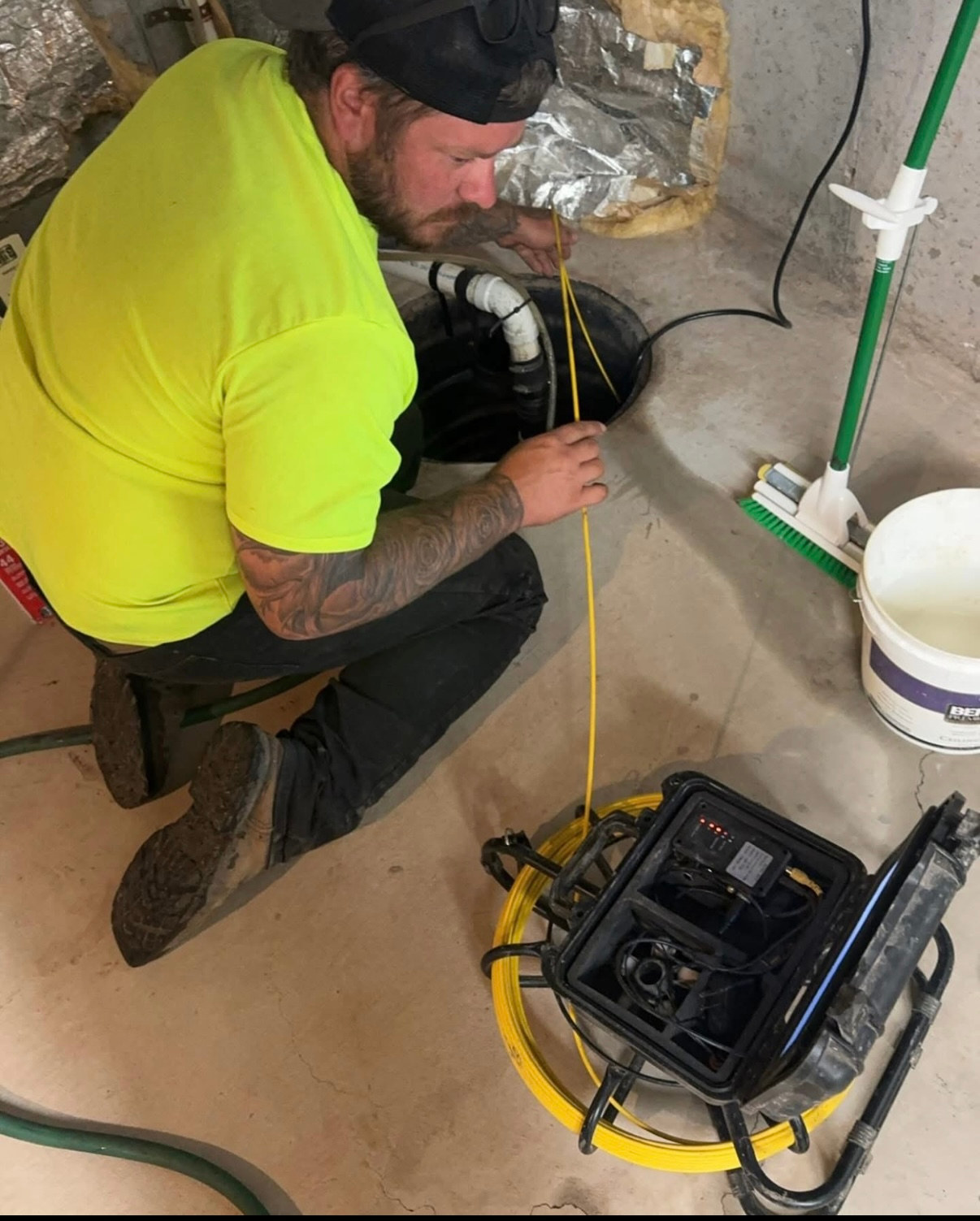 A man in a yellow shirt is working on a drain