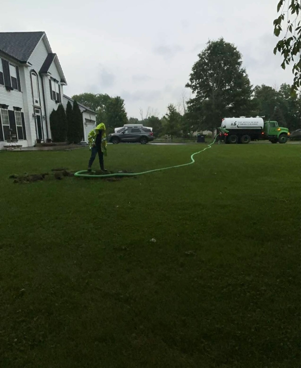 A man is watering a lawn with a hose in front of a large house.