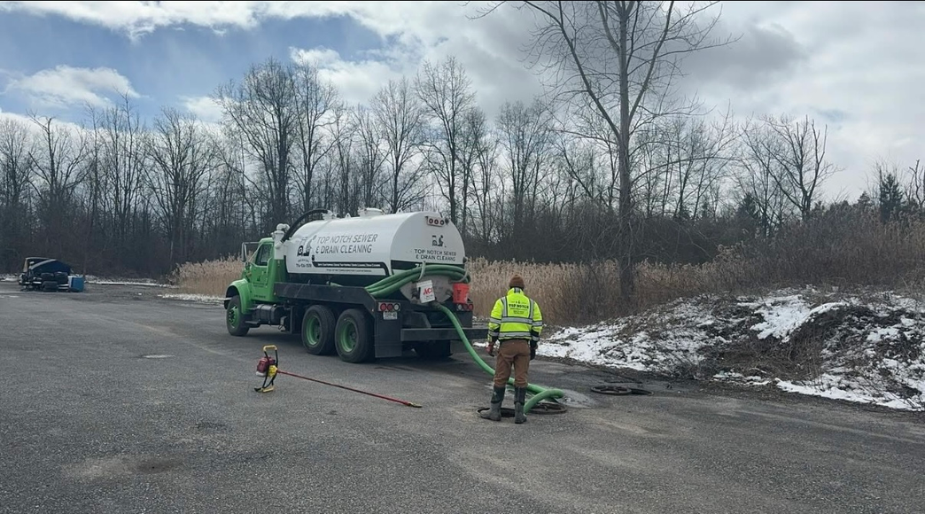 A man is standing next to a vacuum truck on the side of the road.