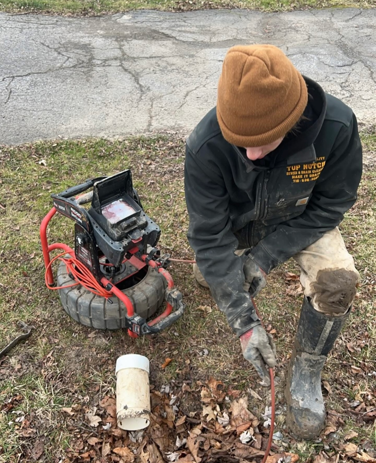 A man is kneeling down next to a drain camera.