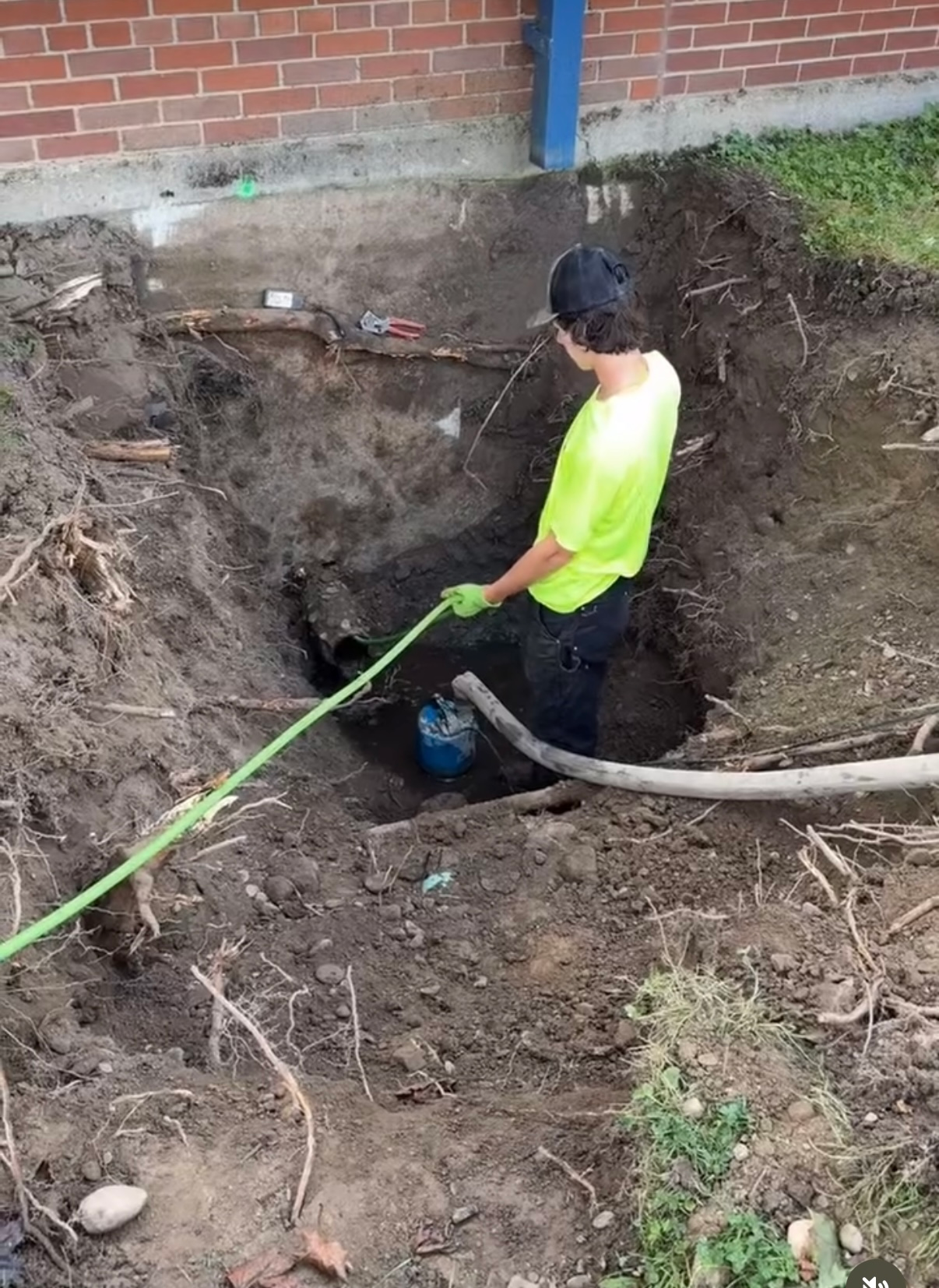 A man is digging a hole in the ground with a hose.