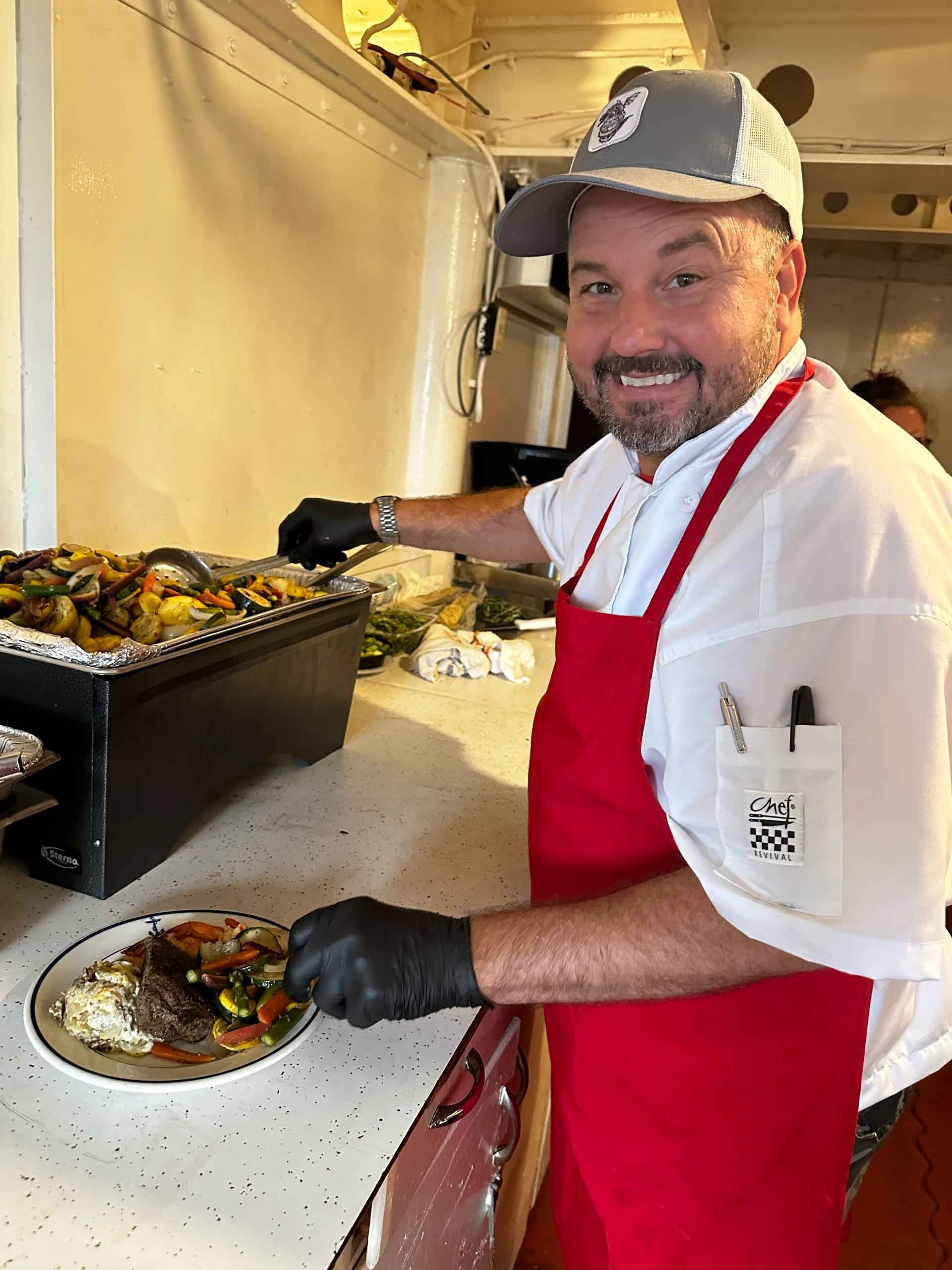 A man in a red apron is preparing food in a kitchen.