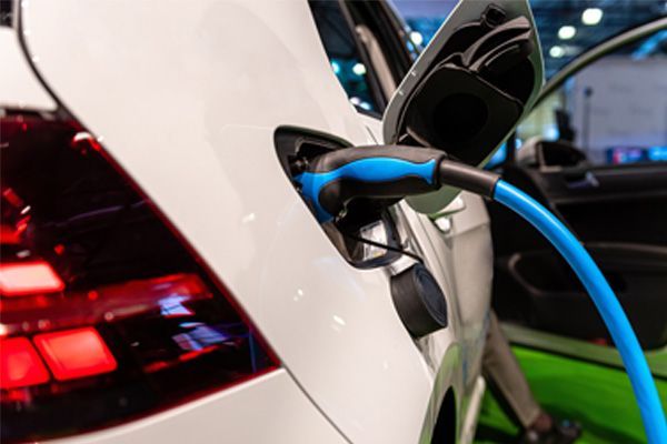 Electric car charging with blue cable plugged into white vehicle at a charging station