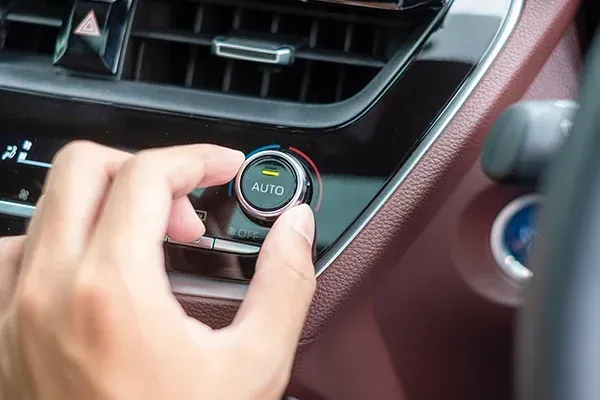 Hand adjusting a car climate control knob near the dashboard vents, with a red trim interior.
