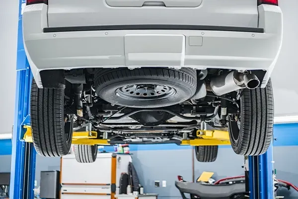 Car undercarriage on a lift in an auto repair shop, showing the rear axle and exhaust.