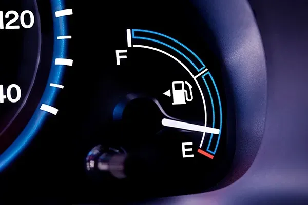 Car dashboard fuel gauge near empty, with fuel pump icon and red warning zone.