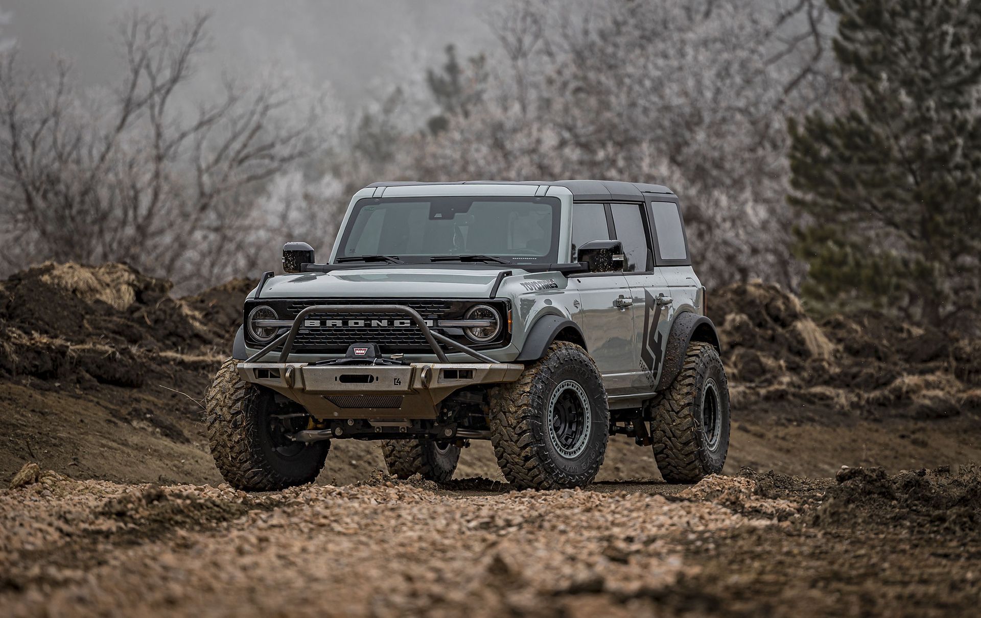 Gray off-road SUV on a muddy trail in a leafless woodland setting